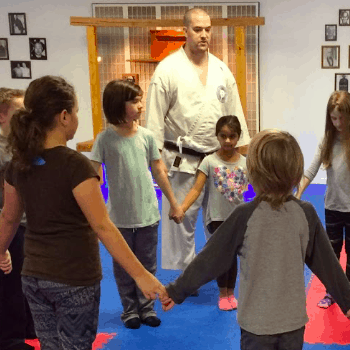 Children and a Martial Arts Teacher gathering together holding hands.